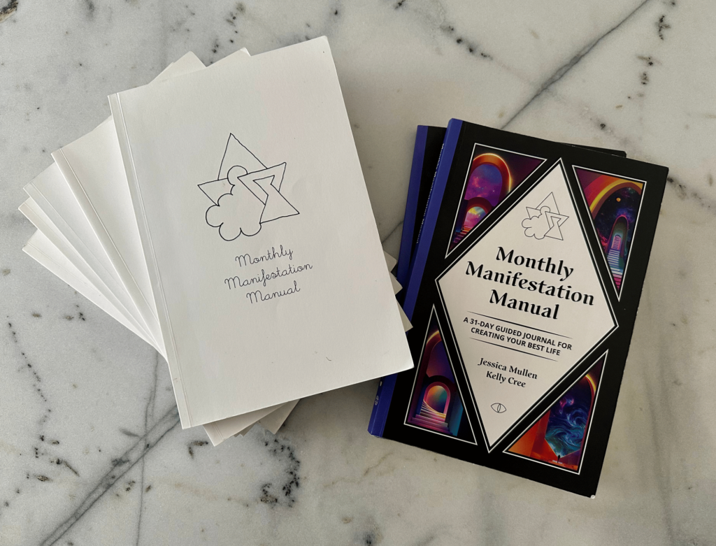 Copies of the monthly manifestation journal by School of Life Design on a marble table. Here are magical tools to change consciousness at will. 